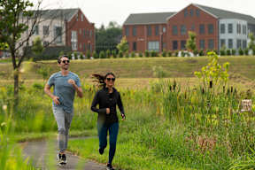 Two people running on a path in a grassy field.