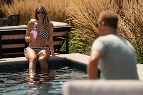 A woman in a striped bikini sits on the edge of a pool holding a drink.