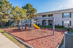 A playground with a slide and swings in front of a building.