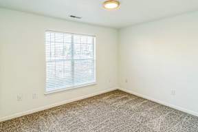 A room with a carpeted floor and a window with blinds.