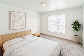 A bedroom with a bed, a plant, and a framed artwork on the wall.