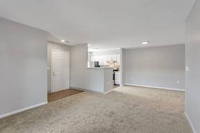 the living room and kitchen of an empty home with a carpeted floor