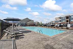 A swimming pool surrounded by a black fence and lounge chairs.