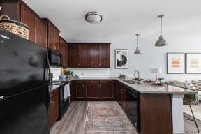 a kitchen with black appliances and wooden cabinets and a rug at the vue apartments in indianapolis