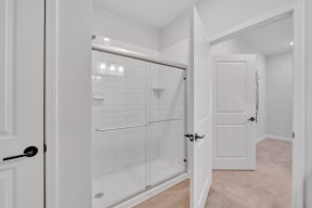 a white bathroom with a shower and a door at spire apartments in charlotte nc