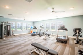 Fitness room with treadmills a bench and elliptical at Trillium apartments in Melbourne fl