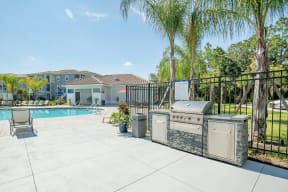 Grill with a palm tree and pool in the background at Trillium apartments in Melbourne fl