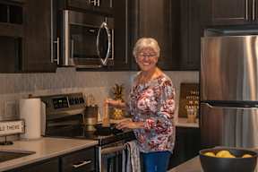 A woman in a floral shirt is cutting a pineapple in a modern kitchen.