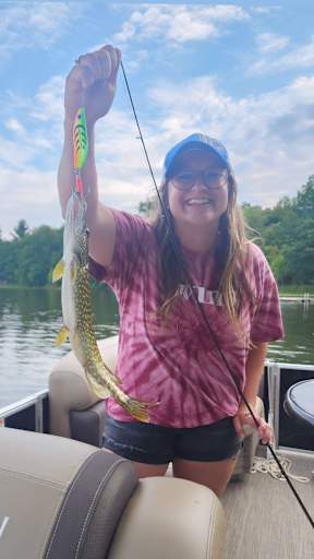 A woman in a pink shirt is holding a fishing rod with a fish on it.