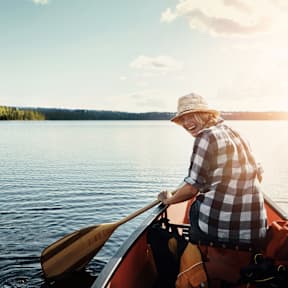 A person wearing a hat is paddling a canoe on a lake.