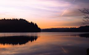 A serene lake with a forest in the background and a sky painted with hues of sunset.
