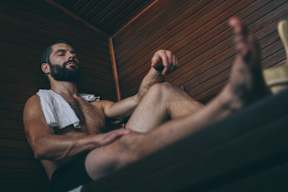A man with a towel wrapped around his neck is sitting in a wooden room.