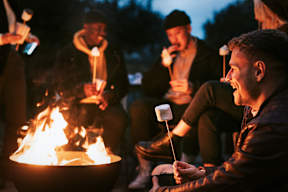 A group of people sitting around a fire with marshmallows on sticks.