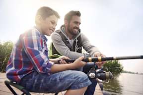 A man and a boy are fishing together on a dock.