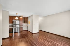 an empty living room and kitchen with wood flooring and white walls