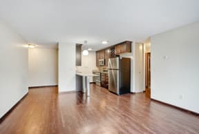 an empty living room and kitchen with wood flooring and a stainless steel refrigerator