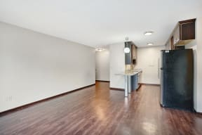 an empty living room and kitchen with wood flooring and a refrigerator