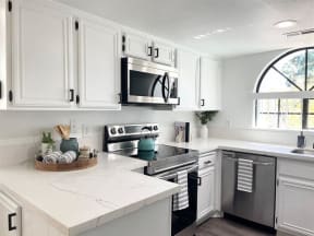 a white kitchen with stainless steel appliances and white cabinets  at The Resort at Encinitas Luxury Apartment Homes, California