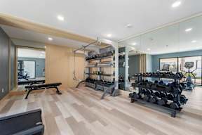 A spacious gym with a variety of equipment including a bench, weights, and a mirror at Latitude Apartments at Mission Valley Apartments, San Diego, California