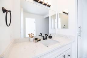A white bathroom with a marble counter top and a round mirror.
