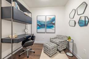 A room with a grey chair, a desk, and a painting on the wall.