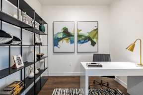 A room with a white desk, black chairs, and two framed artworks on the wall.