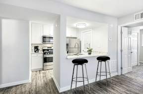 A kitchen with white cabinets and a bar area with black stools.