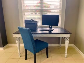 a desk with a computer and a blue chair in front of a window