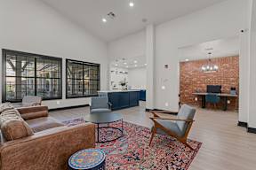 A living room with a brown leather couch, a grey armchair, a round table, and a red and blue ottoman.