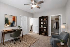 A room with a desk, chair, and a ceiling fan.