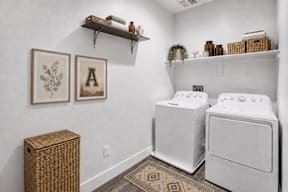 A laundry room with a washer and dryer, a basket, and two framed pictures on the wall.