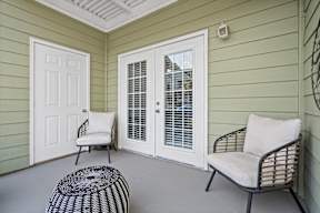 A patio with a chair, ottoman, and sliding door.