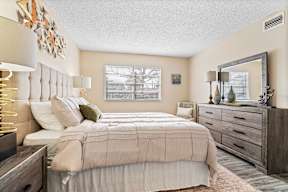 A bedroom with a large bed, a mirror, and a wooden dresser.