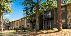 A row of apartment buildings with trees in front.
