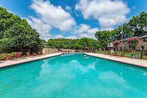 A large swimming pool surrounded by trees and lawn chairs.
