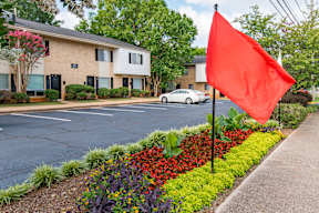 A red flag is flying in front of a building with a white car parked in front.