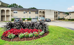 A flower bed with red flowers in front of apartment buildings.