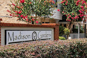A sign that says "Madison Gardens" in front of a building.