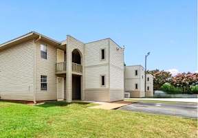 A beige two-story apartment building with a parking lot in front.
