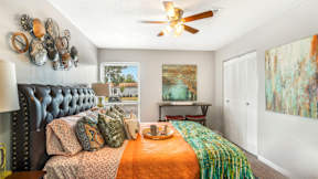 A bedroom with a black headboard and a bed with orange and green bedspread.