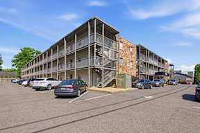A parking lot with cars and a multi-story building with balconies.