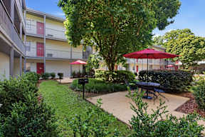 A red umbrella is on a patio table in a courtyard.