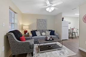 A living room with a grey sofa, a black and white checkered chair, a coffee table, and a ceiling fan.
