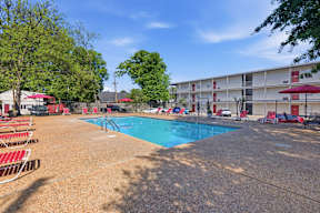 A swimming pool surrounded by red chairs and trees.