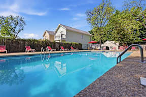 A swimming pool with red chairs and a building in the background.