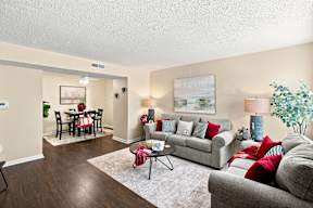 A living room with a grey couch, a coffee table, a dining table with chairs, and a painting on the wall.