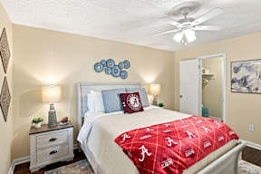 A bedroom with a bed covered in a red Alabama football bedspread.