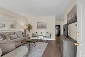 A living room with a grey couch, a coffee table, a chair, a painting, a vase, and a television.