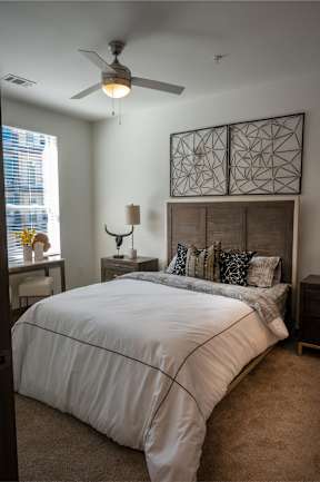 A bedroom with a bed, nightstand, and a ceiling fan.