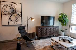 A black chair sits in a living room with a large abstract painting on the wall.